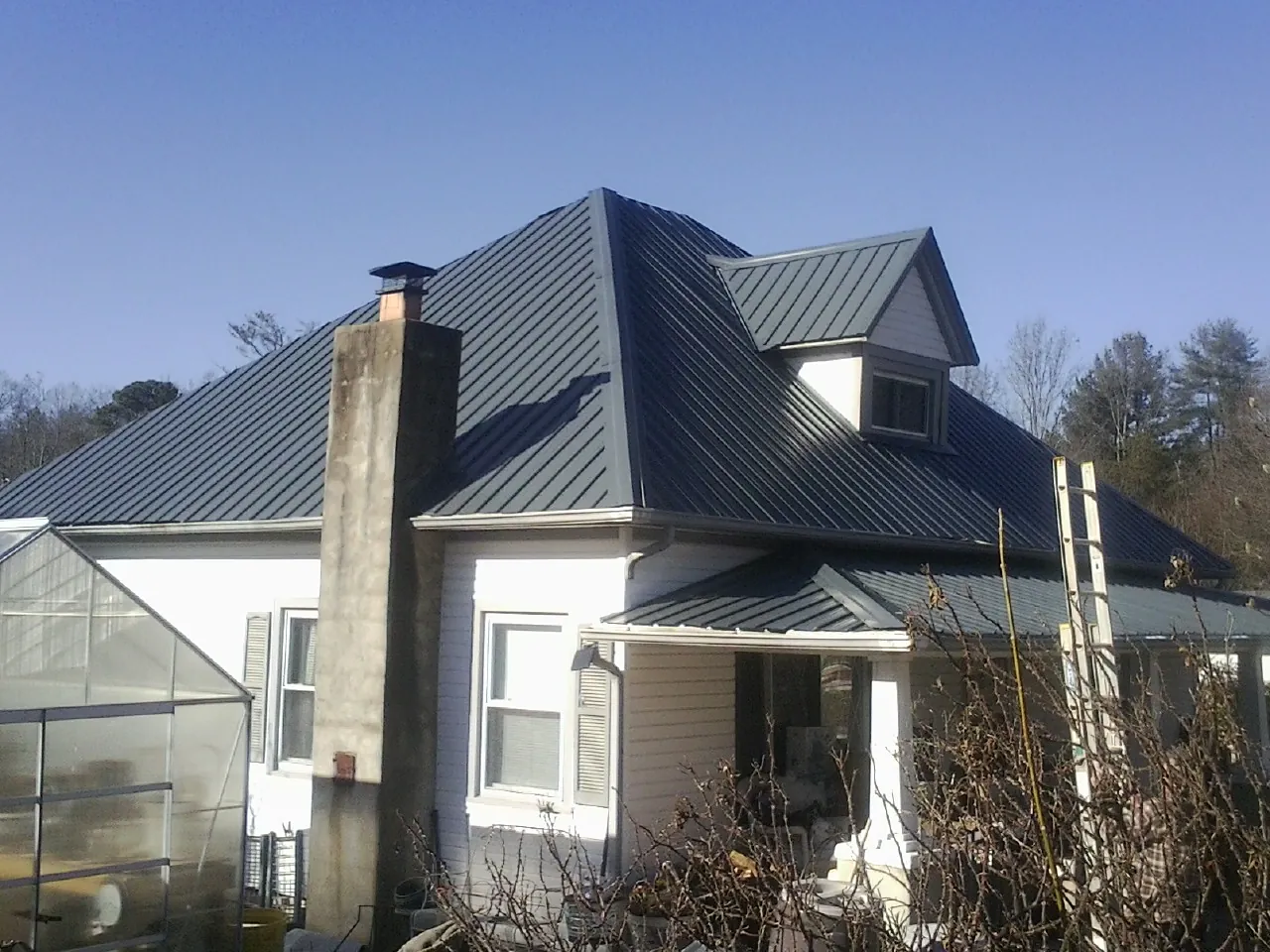 Dark blue standing seam metal roof on a white farmhouse with dormer — Slate & Tile Roof Repair by Roofing Brothers in Ellerbe