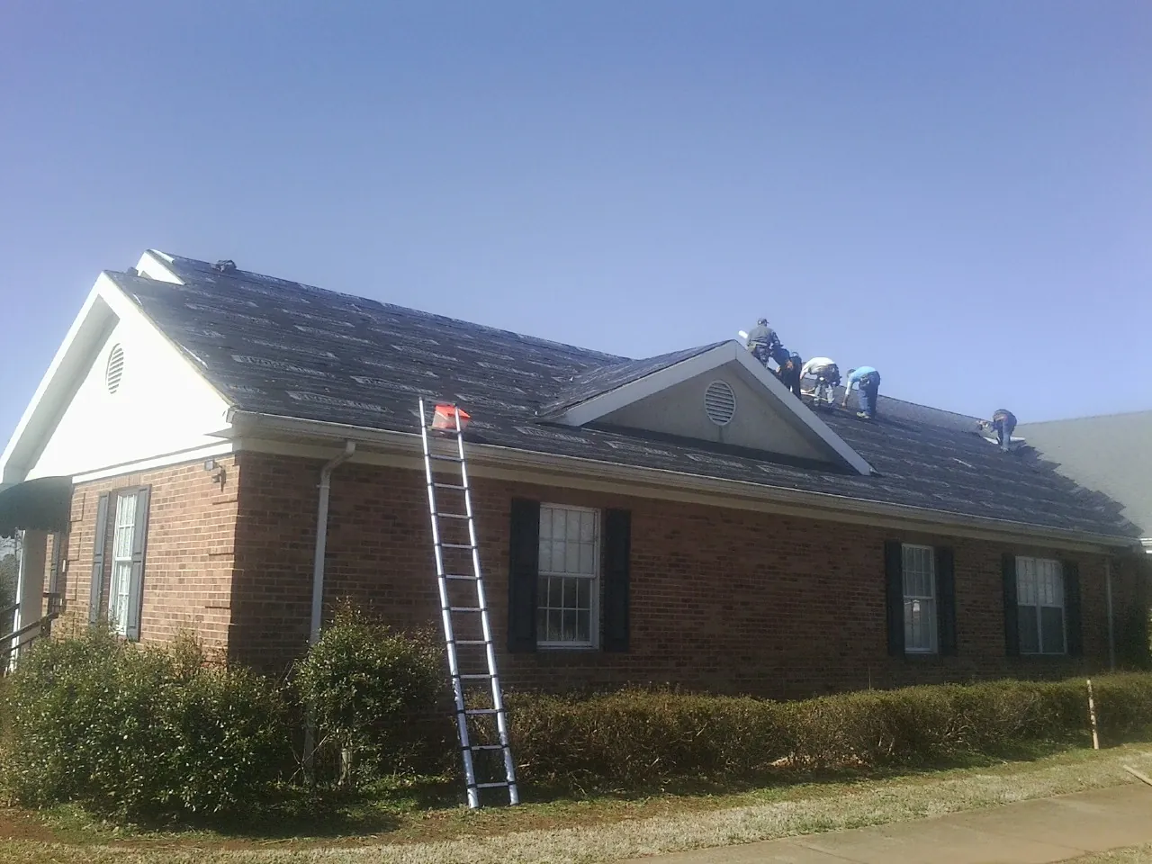 Crew tearing shingles off a brick ranch roof with a ladder set — Emergency Roof Repair work by our crew in Ellerbe