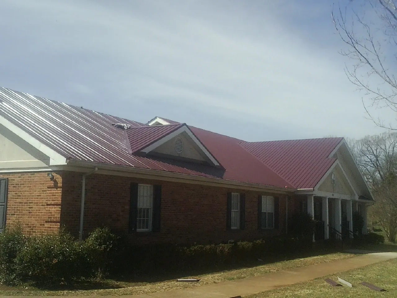 Red metal roof with gabled entries on a long brick building, from a Hail Damage Roof Repair job in Ellerbe