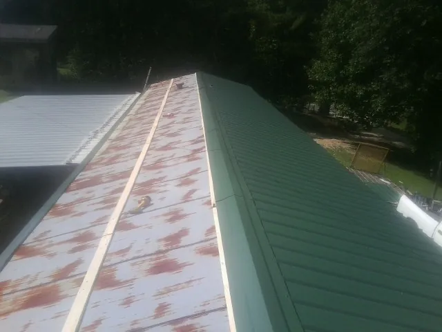 Old rusted panels beside newly installed green metal roofing — Wind Damage Roof Repair by Roofing Brothers in Ellerbe