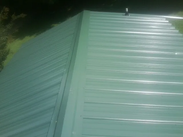 New green metal panels meeting at the ridge of a roof — Flat Roof Repair work by our crew in Ellerbe