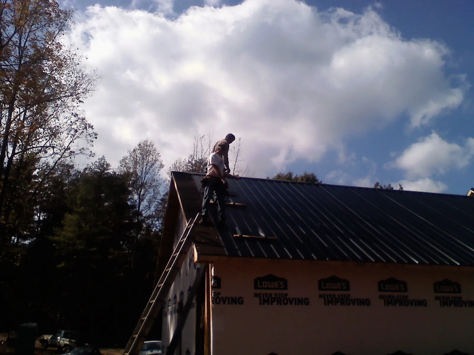 Roofer fastening dark metal panels high against a cloudy sky, from a Roof Inspection job in Ellerbe