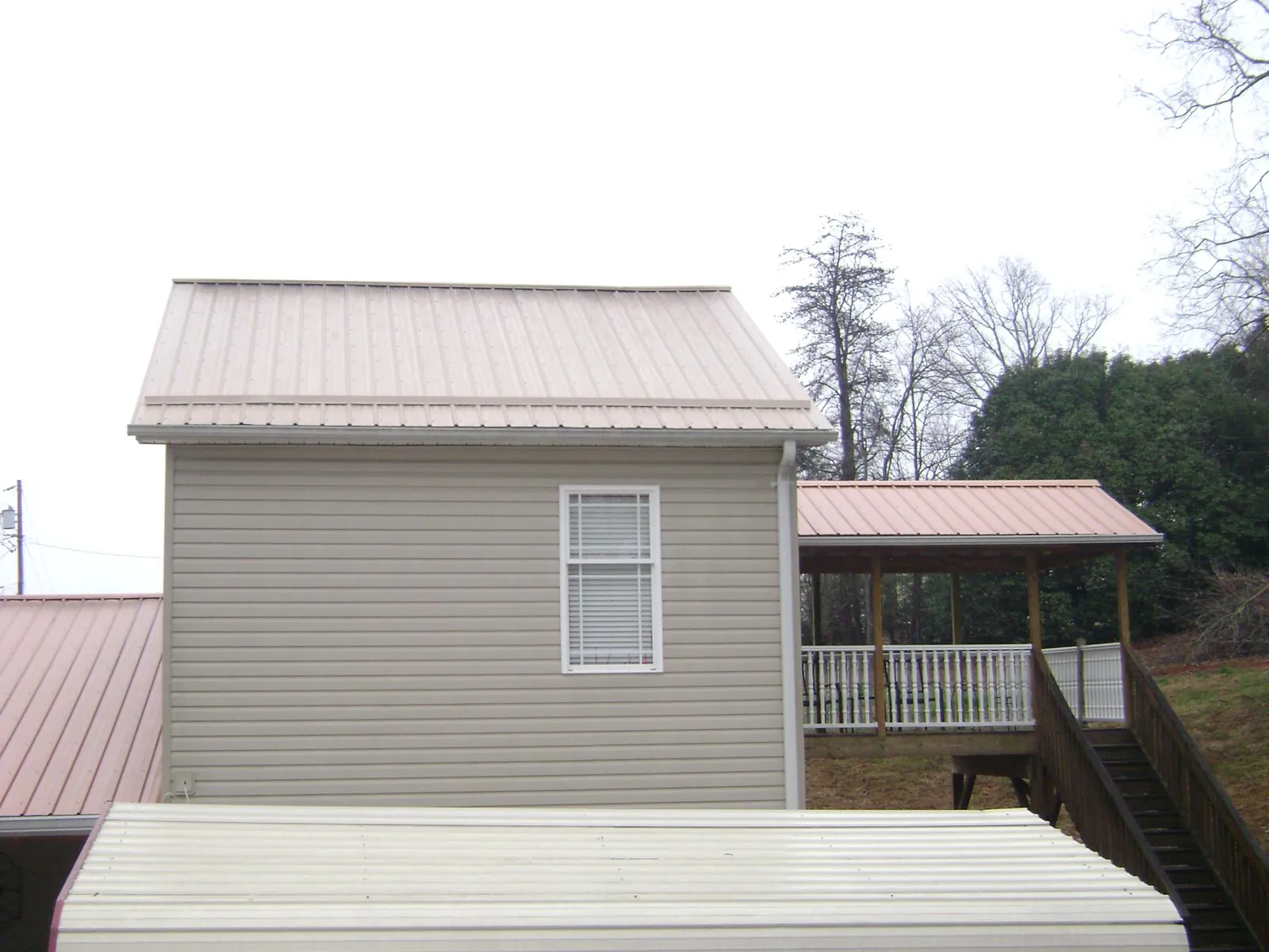 Tan metal roofs on a two story addition and attached porch, from a Roof Replacement job in Ellerbe